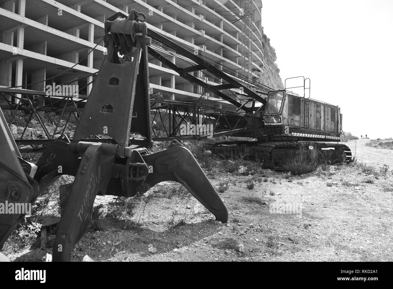 Foto in bianco e nero di gru abbandonate di fronte hotel incompiuta in Montenegro. Macchina arrugginita e vuoto edificio abbandonato. Foto Stock
