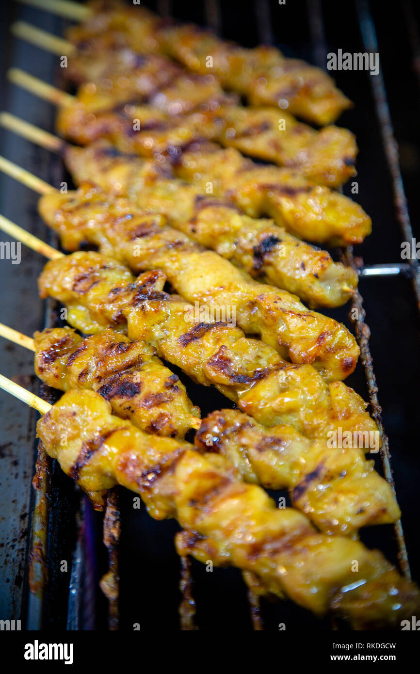 Pollo satay su spiedini di bambù per la cottura su una griglia in un mercato thailandese stallo. Satay è un piatto di agguerriti, infilzato e carne alla brace, servita con un sauc Foto Stock