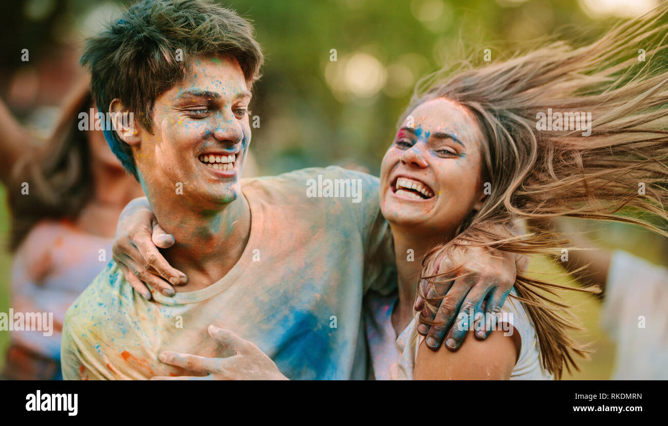 L uomo e la donna con le loro facce cosparse di holi colori aventi il divertimento all'aperto. Coppia felice azienda ogni altra riproduzione di holi con i loro amici in un par Foto Stock