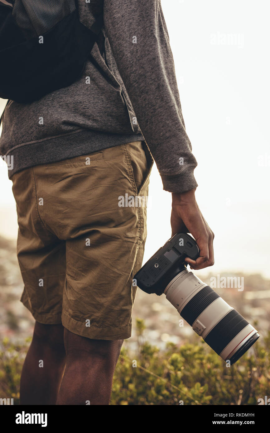 La sezione centrale colpo di uomo in piedi all'aperto con la sua reflex digitale con obiettivo zoom. Fotografo escursionismo in natura per i nuovi contenuti per il suo social media. Foto Stock