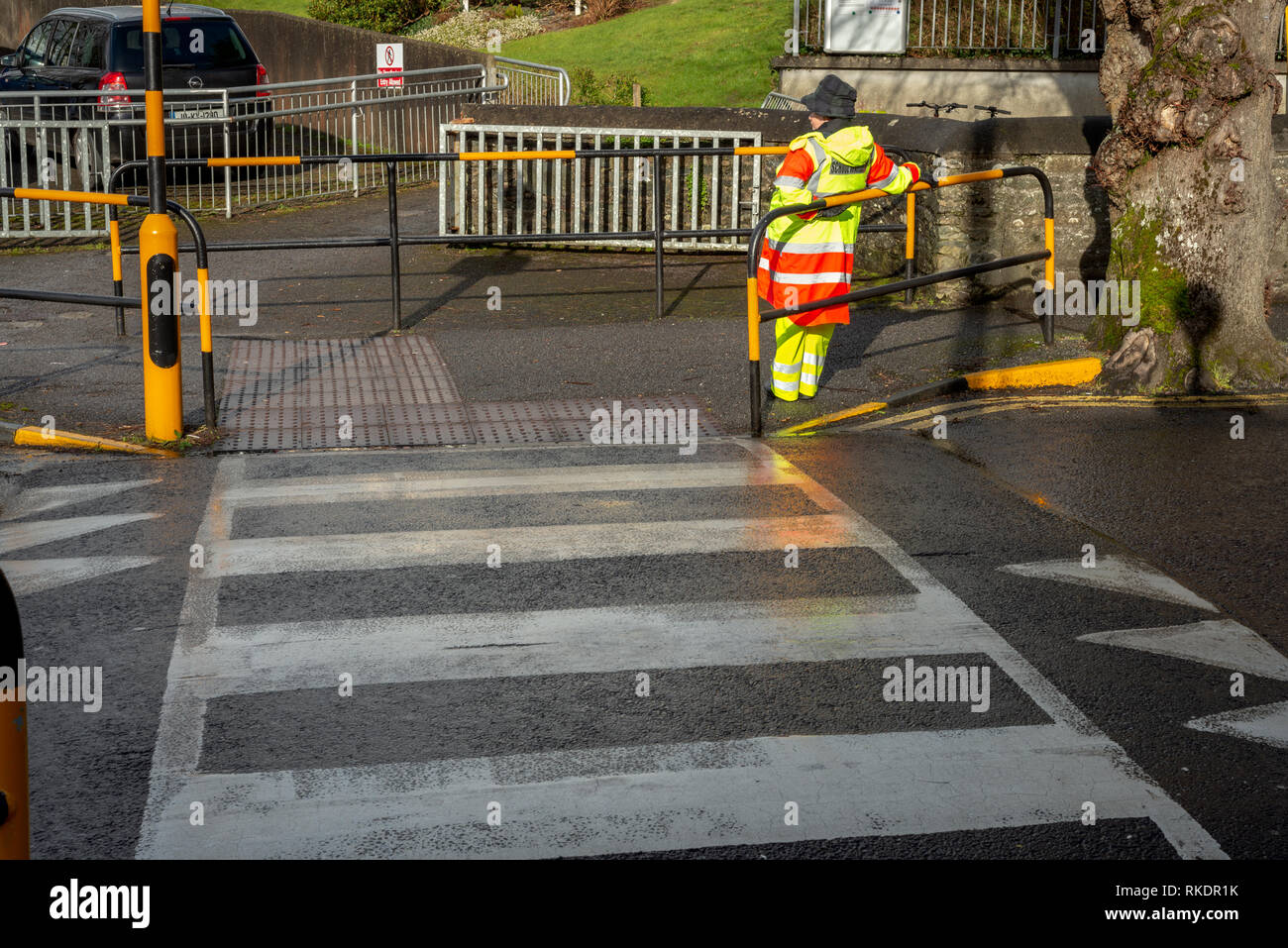Lollipop lady School traffico in attesa di un crosswalk per aiutare gli studenti che attraversano la strada a New Road, Killarney, County Kerry, Irlanda Foto Stock