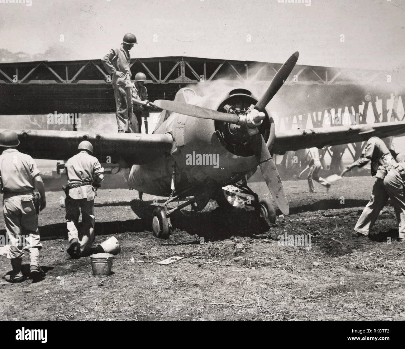 Marine da combattimento aereo salvata. Mise in fiamme da una bomba giapponese ha colpito sulla gruccia in background, questo Marine fighter piano è stato tirato in aperta da Leatherneck che hanno utilizzato la sporcizia e le sostanze chimiche per estinguere le fiamme. Il piano, un Grumman â€oeWildcatâ€ non fu danneggiata gravemente ed è stato in grado di tornare all'aria. La foto è stata scattata poco dopo i Marines catturato una strategica Guadalcanal aeroporto dal giapponese. 1942 Foto Stock