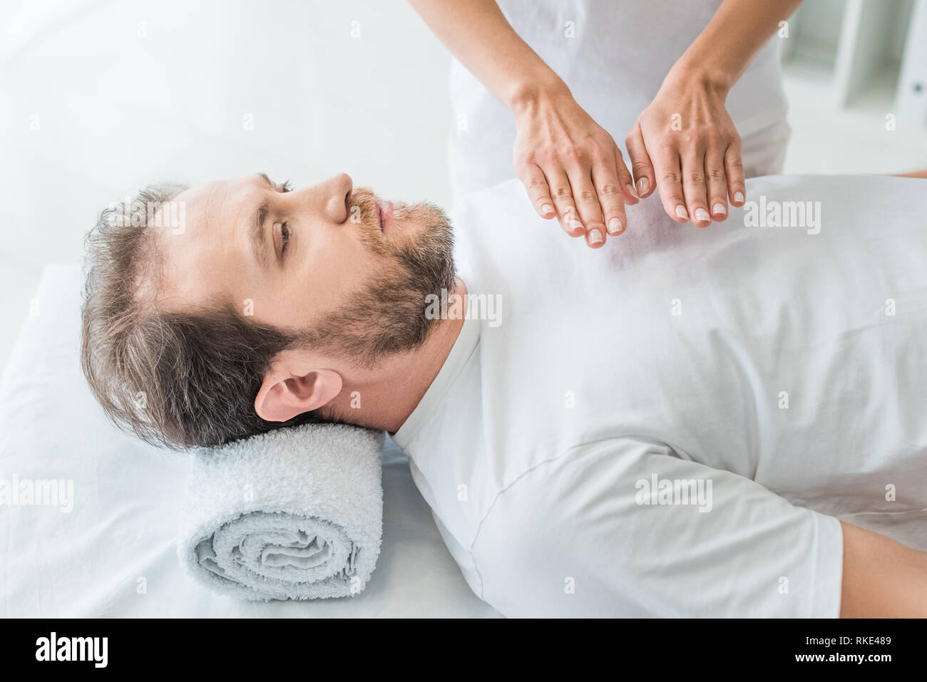 Angolo di alta vista di uomo barbuto ricevendo trattamento reiki Foto Stock
