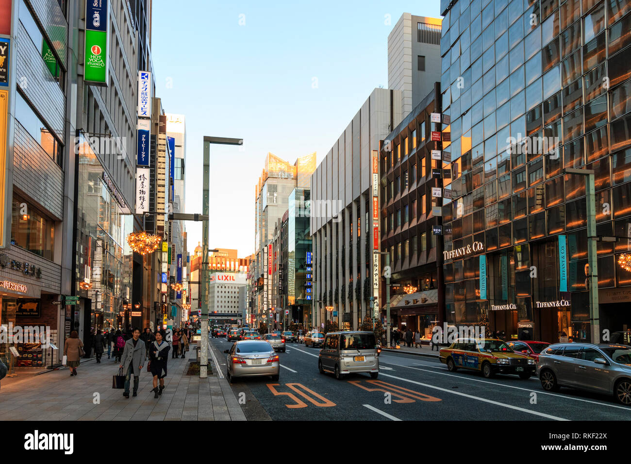 Tokyo, il Ginza. Ora d'oro. Vista lungo la strada con Tiffany store in primo piano. Alberi di Natale sulla strada, il traffico e le persone. Foto Stock