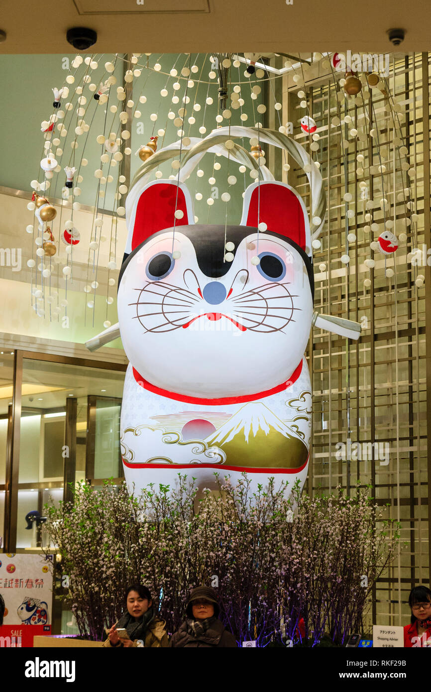 Tokyo, Ginza. Due coppia donne giapponesi seduti nella parte anteriore del gigante gonfiato lucky cat all'interno della lobby all'entrata del negozio di lusso da shopping contatore advisor Foto Stock