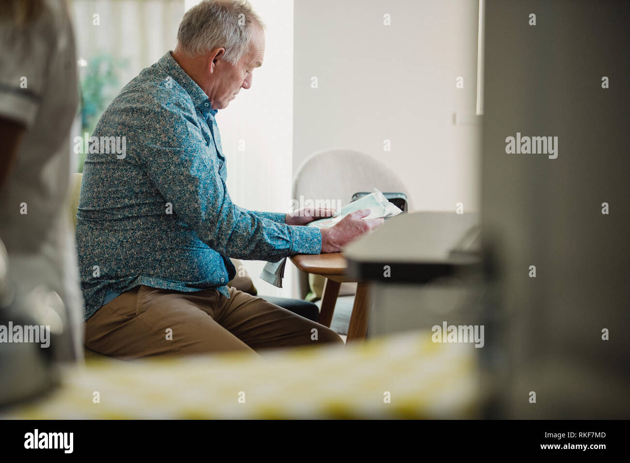 Senior uomo diabetici è seduta al tavolo da pranzo leggendo un giornale mentre il suo caregiver prepara il suo farmaco. Foto Stock