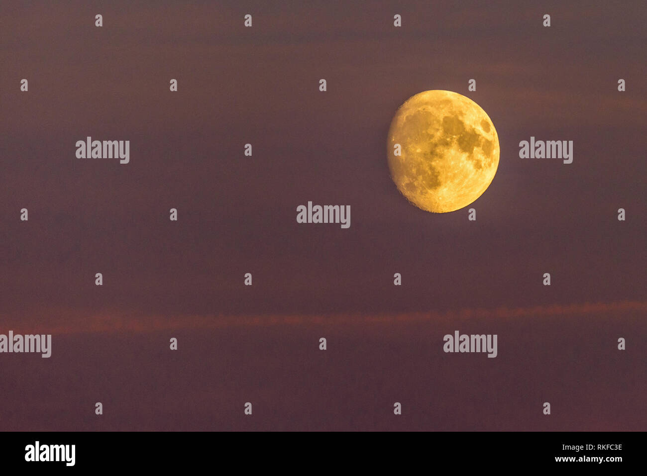 La luna è in aumento contro un colore porpora nello sky tramonto. Un po' di cloud è visibile. Foto Stock