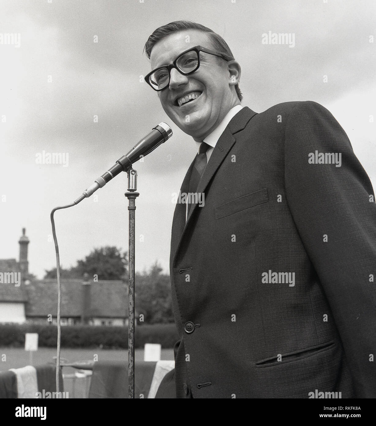 1967, storico, il leggendario entertainer, musicista e presentatore televisivo, Castello di Roy al microfono di un impianto di informazione pubblica in un villaggio di fete, Buckinghamshire, Inghilterra, Regno Unito. I suoi bambini programma televisivo "Record Breakers", è stato uno dei più popolari e di lunga esecuzione di programmi di questa epoca. Foto Stock