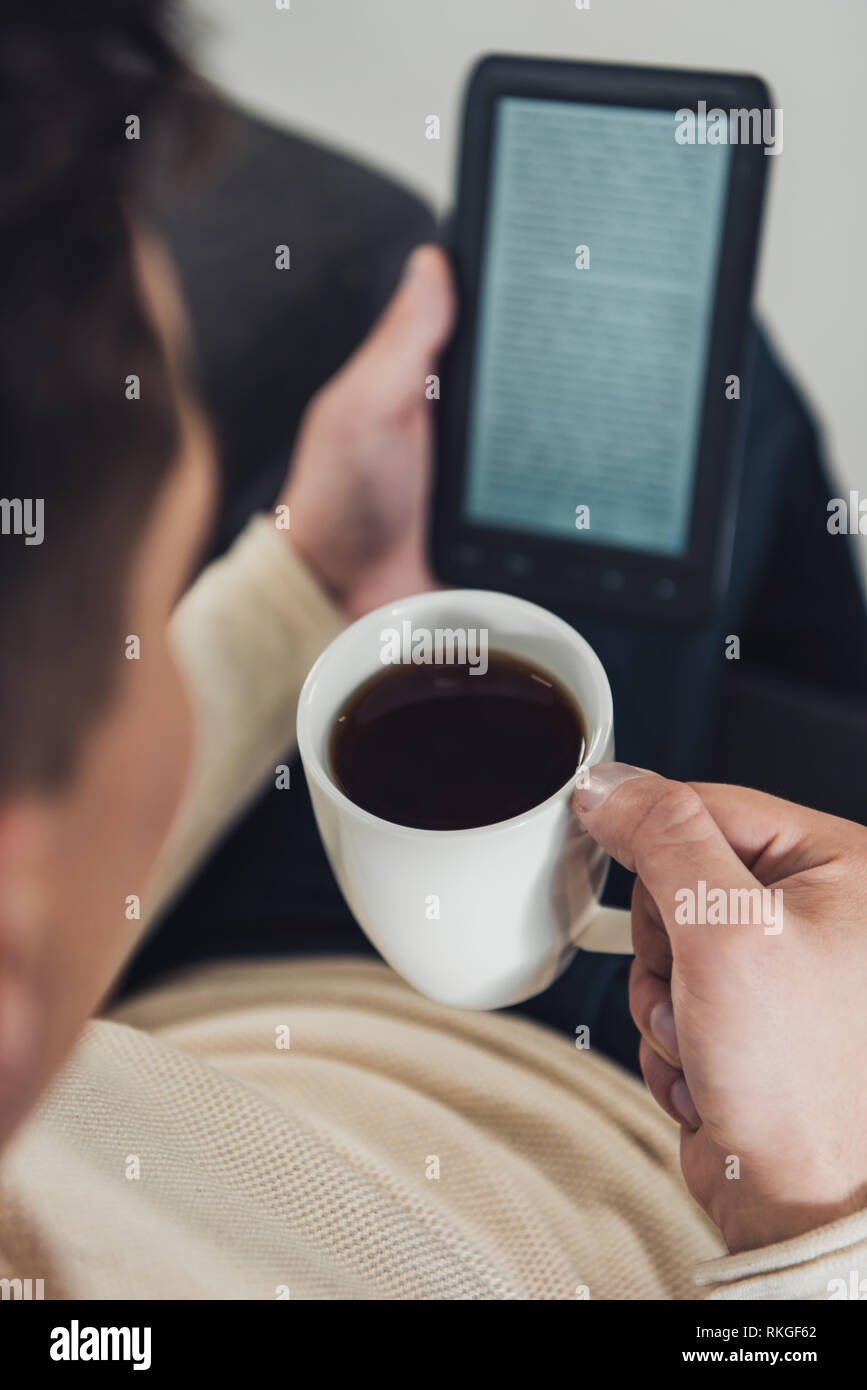 Messa a fuoco selettiva del bicchiere con la bevanda in mano di uomo la lettura di ebook Foto Stock