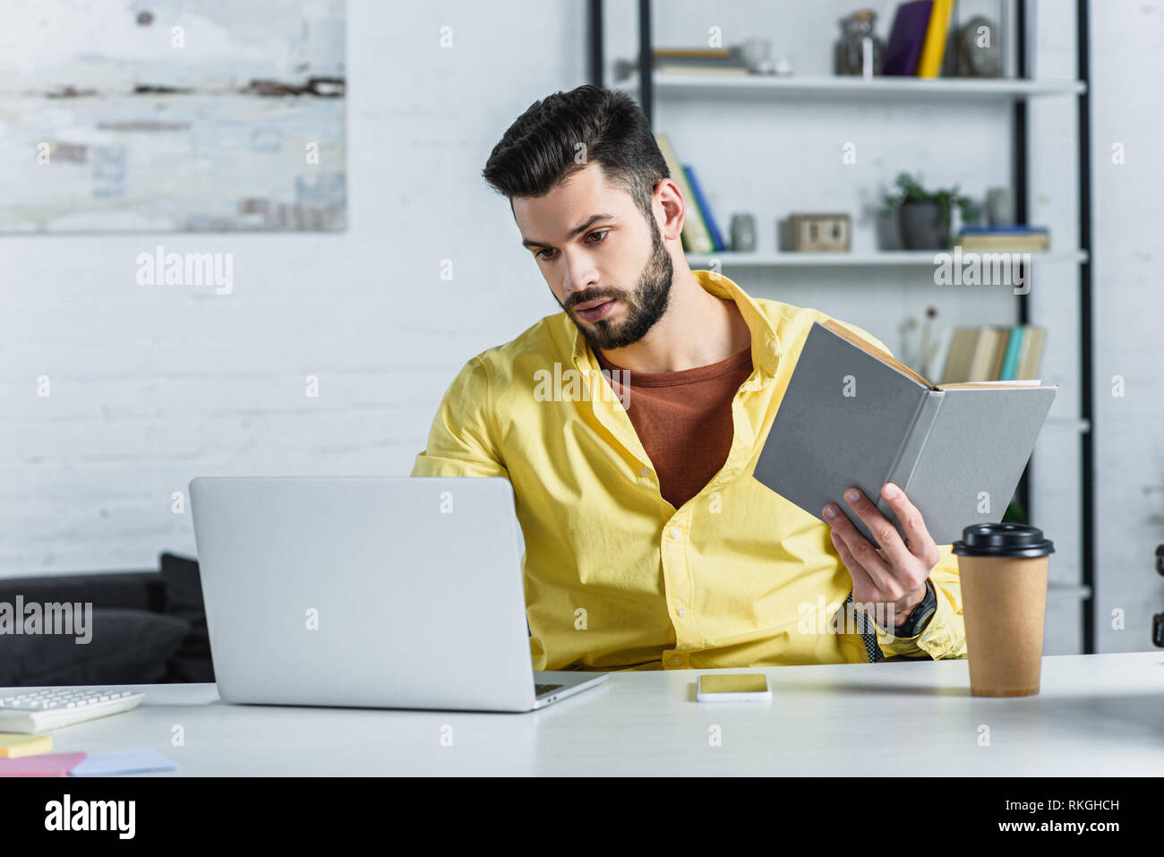 Concentrato imprenditore barbuto guardando laptop e azienda prenota Foto Stock