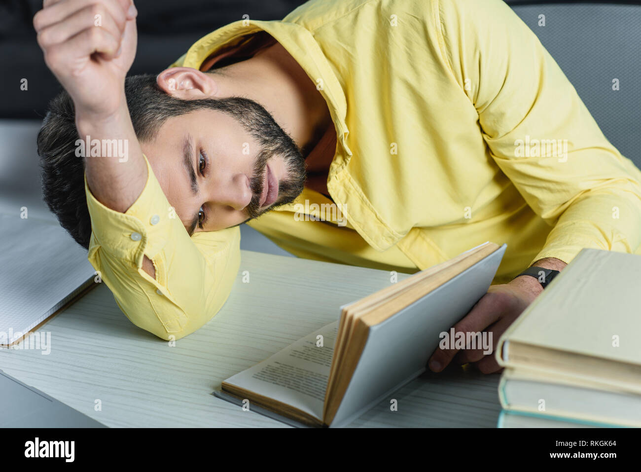 Stanco uomo studiando con libro mentre giaceva sul tavolo in ufficio moderno Foto Stock