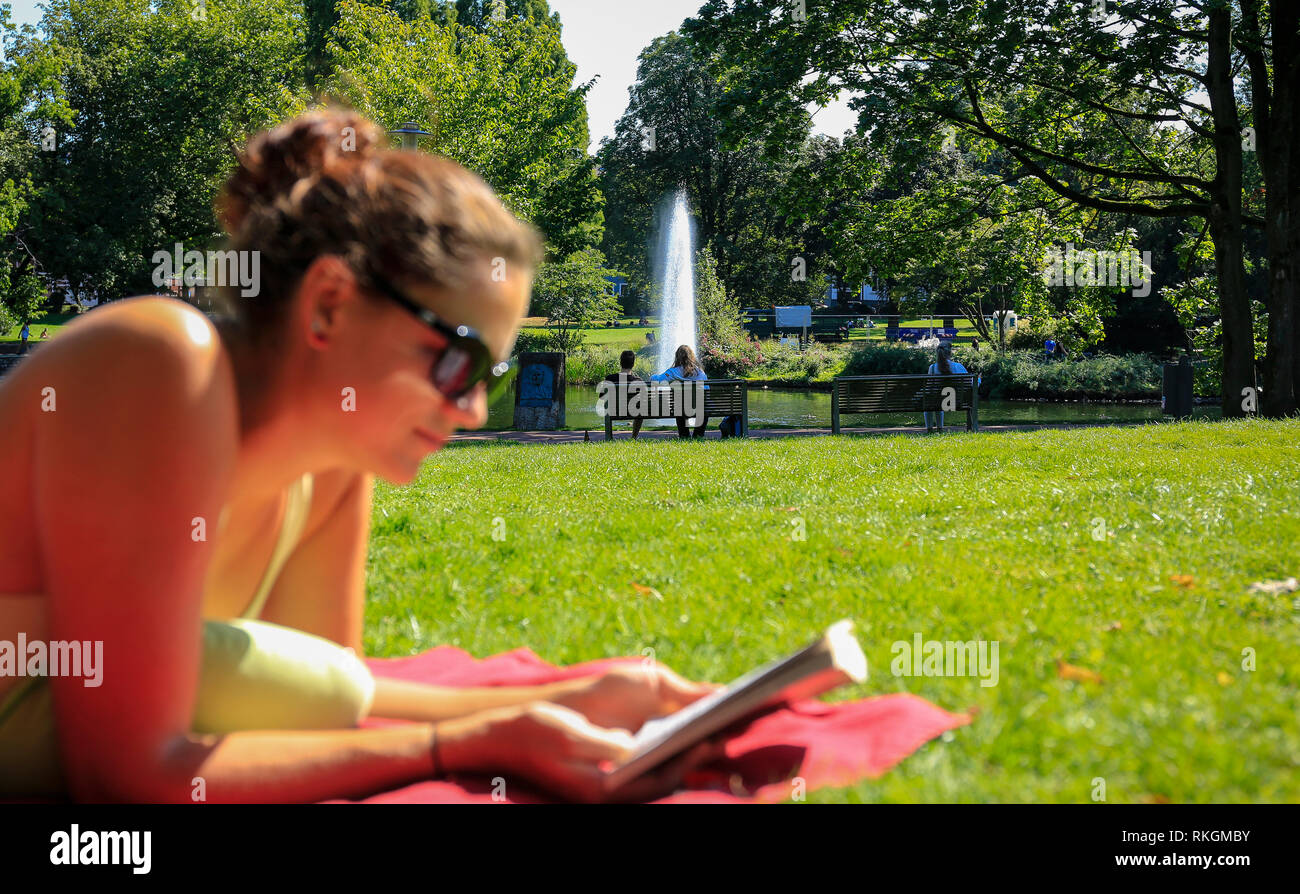 Essen, Renania settentrionale-Vestfalia, la zona della Ruhr, Germania, Essen City Garden, giovane donna giace sul prato e legge in un libro, parco paesaggio con lago e Foto Stock