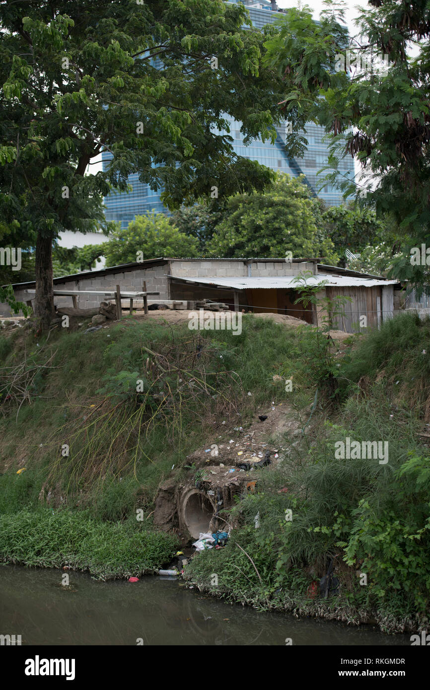 Povertà, drenaggio in fogna aperta con baracca con il Ministero delle Finanze edificio in background, Dili, Timor Est Foto Stock
