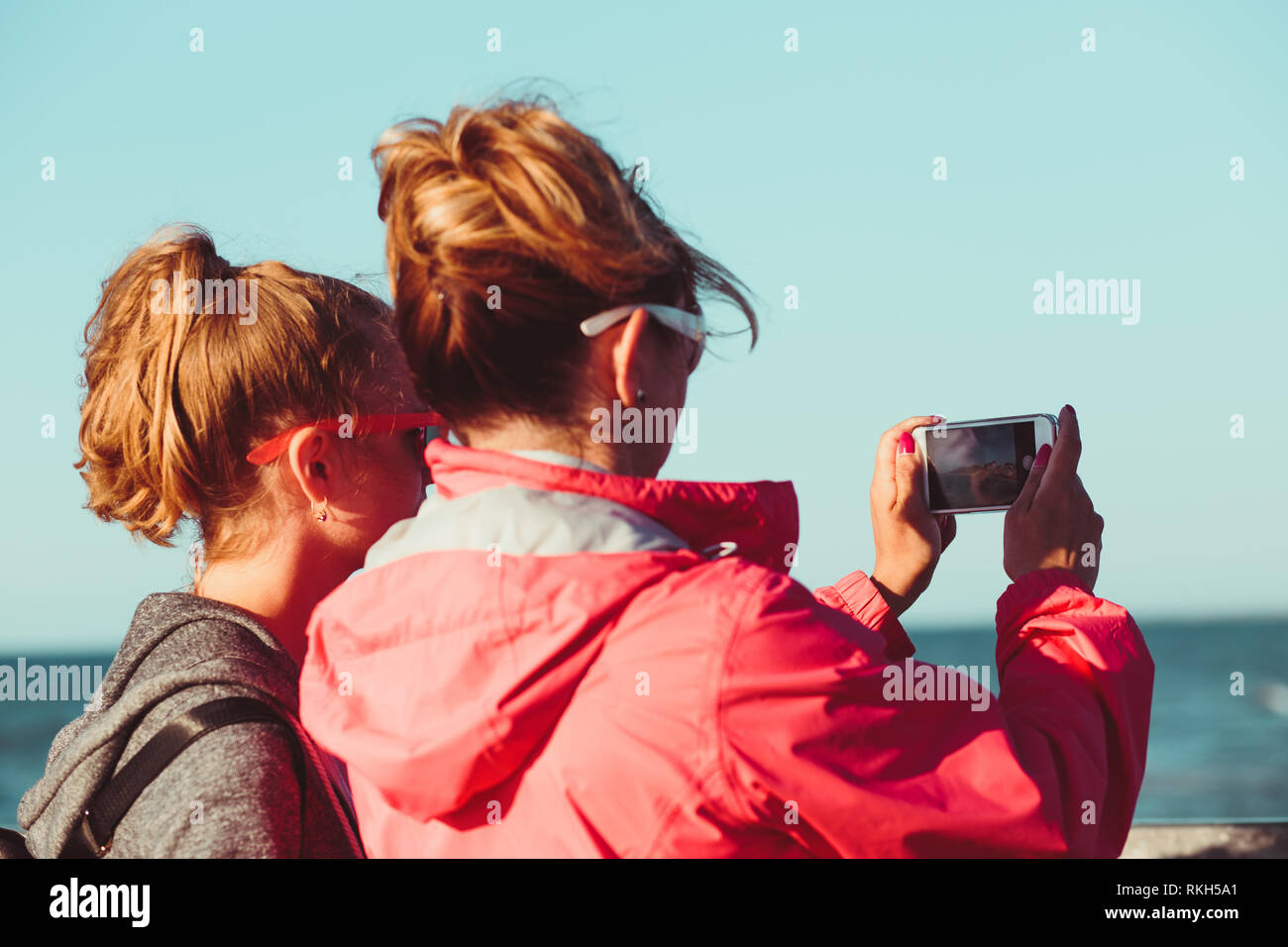 Vista posteriore della madre e figlia di prendere una foto oltre il mare durante le vacanze estive utilizzando la fotocamera dello smartphone Foto Stock