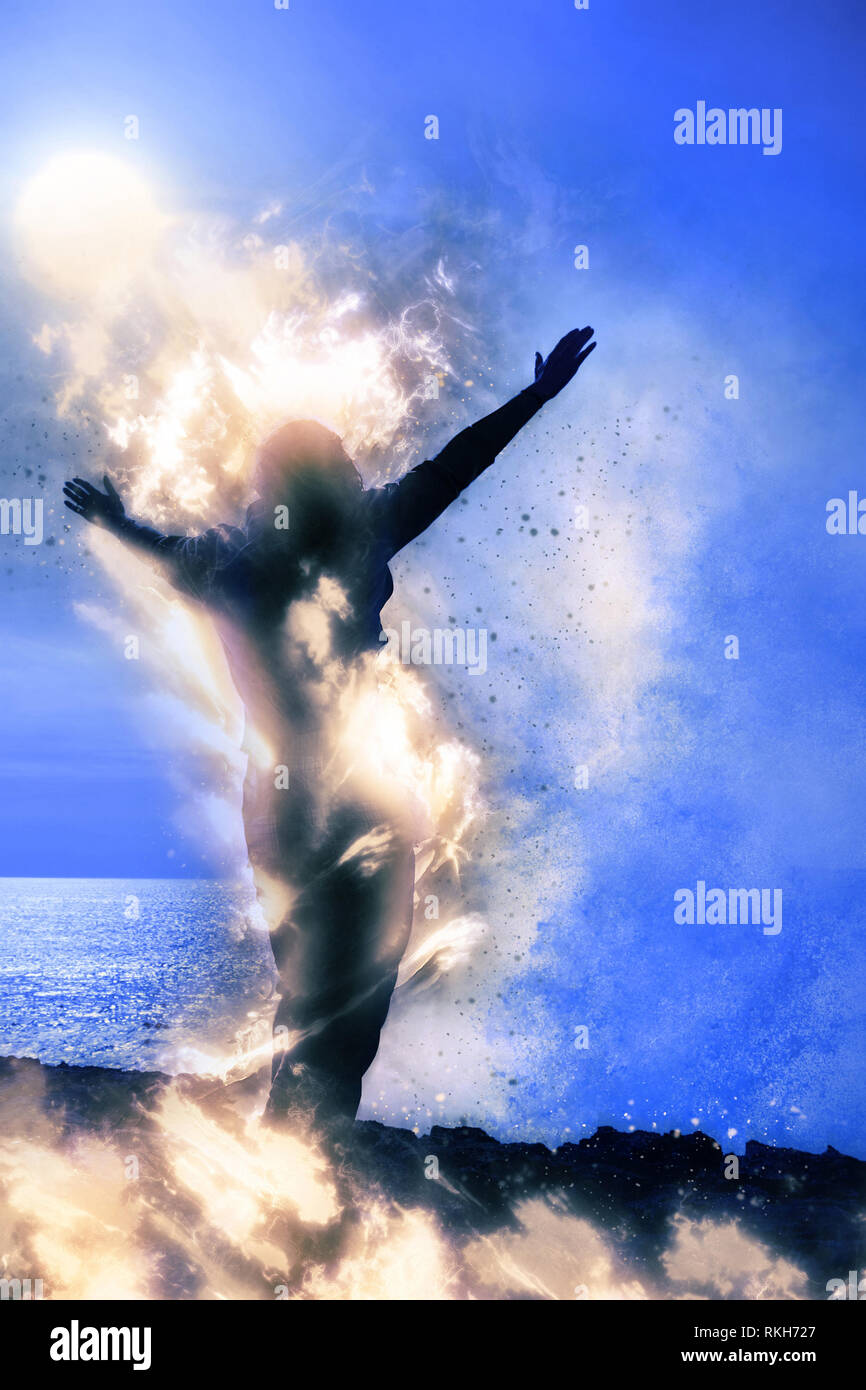 Una donna sola alzando le braccia spiritualmente sul fuoco di fronte a un potente onda a strapiombo sul mare Foto Stock