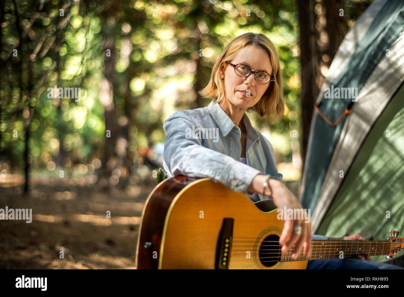 Metà donna adulta a suonare la chitarra mentre il campeggio. Foto Stock