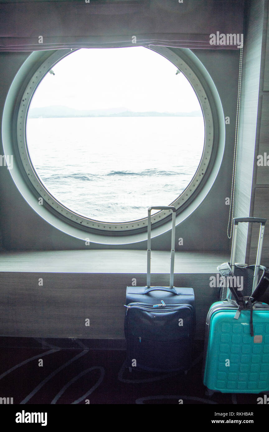 Due valigie per viaggiare nella parte anteriore del round di oblò della nave, il concetto di viaggio di piacere o di lavoro, colpo verticale Foto Stock