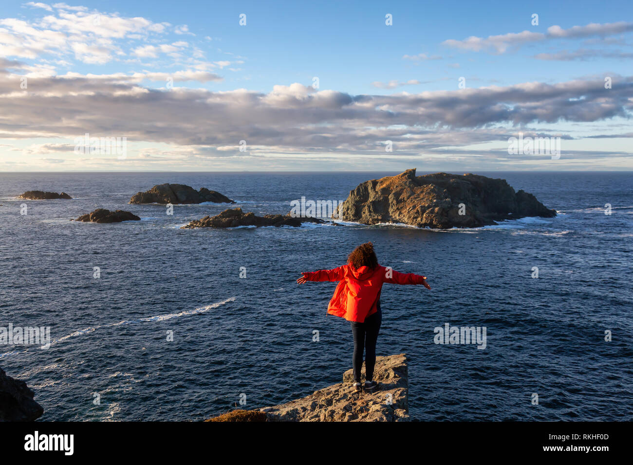 Woman in Red jacket è in piedi sul bordo di una scogliera con le braccia aperte e godere degli splendidi paesaggi dell'oceano. Preso in testa di corvo, Nord Twillingate Foto Stock