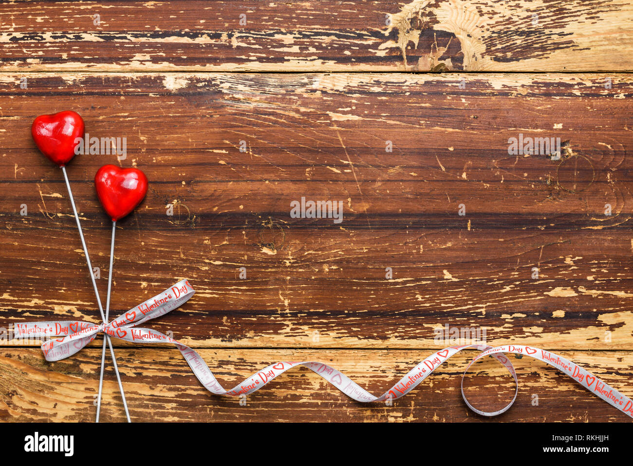 Paio di cuori rossi su bastoni legate con un nastro su un sfondo di legno. Valentines Day card concept. Foto Stock