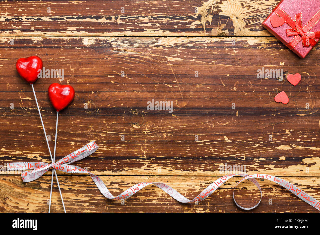 Paio di cuori rossi su bastoni legate con un nastro e confezione regalo su uno sfondo di legno. Valentines Day card concept. Foto Stock