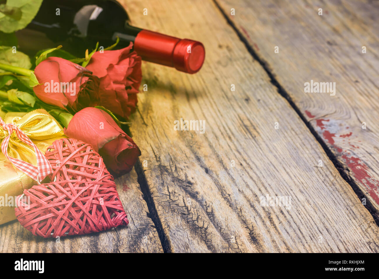 Il giorno di San Valentino del concetto. Cuore di vimini, red rose, confezione regalo e una bottiglia di vino in un ambiente rustico in legno con blackboard copia spazio per il testo. Messa a fuoco selettiva. Foto Stock