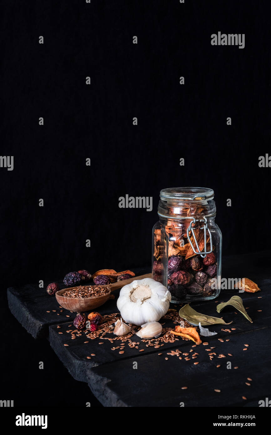 Aglio, frutta secca e semi di rustico scuro dello sfondo. Foto artistiche di aglio e frutta secca in un barattolo sulla vecchia tabella nero girato in chiave di basso ciaroscurr Foto Stock