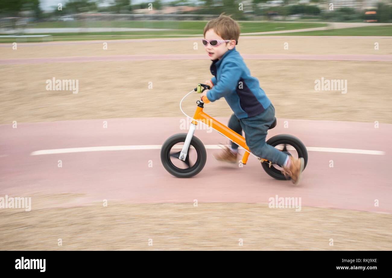 Ragazzo in giacca blu a cavallo di un rapido equilibrio arancione bike o run bike. Sfocato low motion shot. Foto Stock