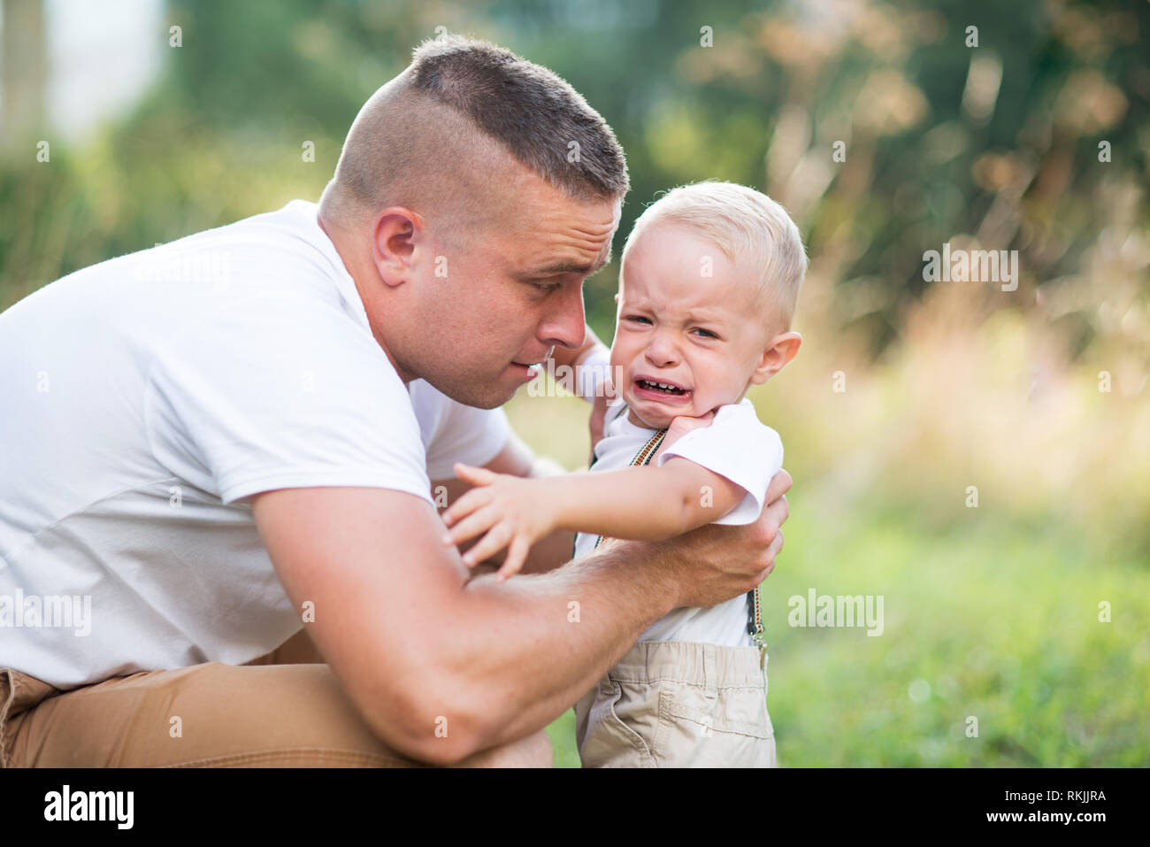 Giovane padre con un piccolo pianto toddler figlio nella soleggiata estate natura. Foto Stock