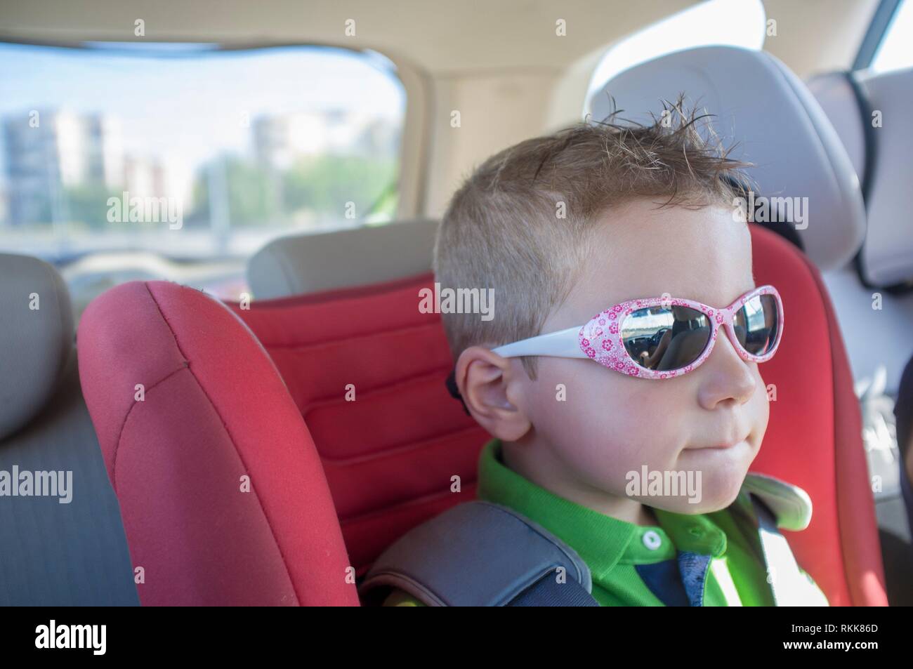 Bambino bello ragazzo che indossa gli occhiali da sole all'interno dell'auto. La protezione degli occhi durante i viaggi in macchina concept. Foto Stock