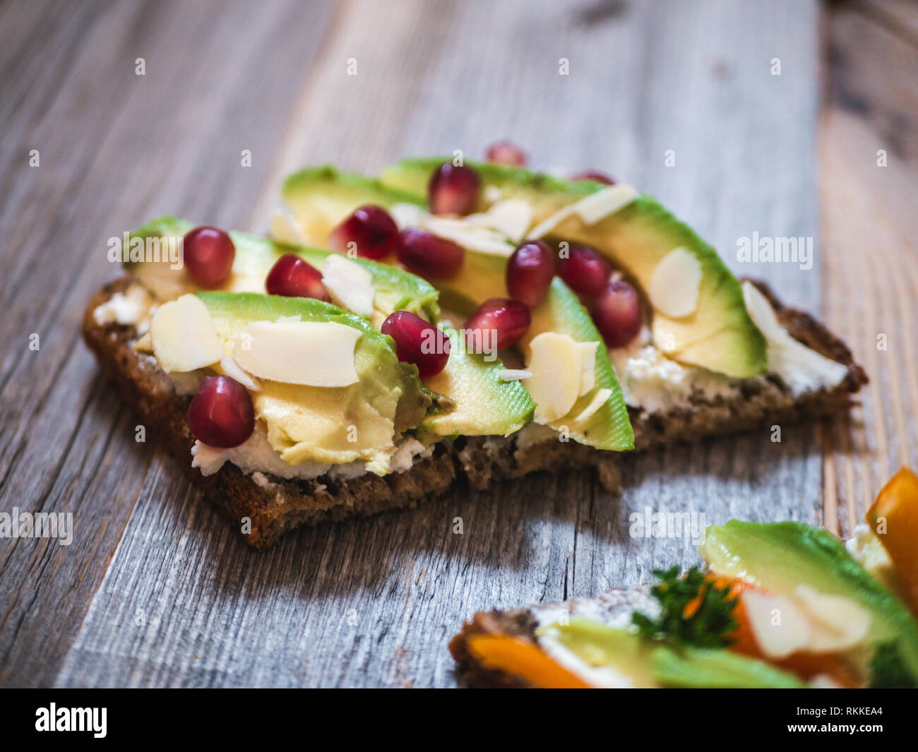 Delizioso e sano avocado toast con melograno, peperone e mandorla rustico di legno Foto Stock