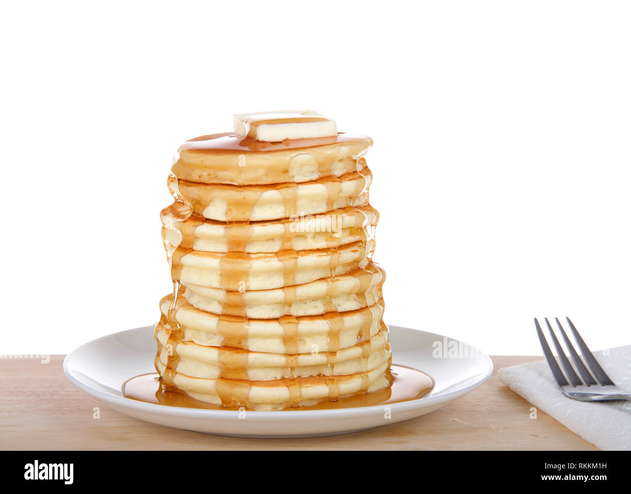 Fluffy pancakes impilati alta, burro e sciroppo, sulla piastra di porcellana sulla luce di una tavola di legno. Forcella e tovagliolo accanto, isolato su bianco. Foto Stock