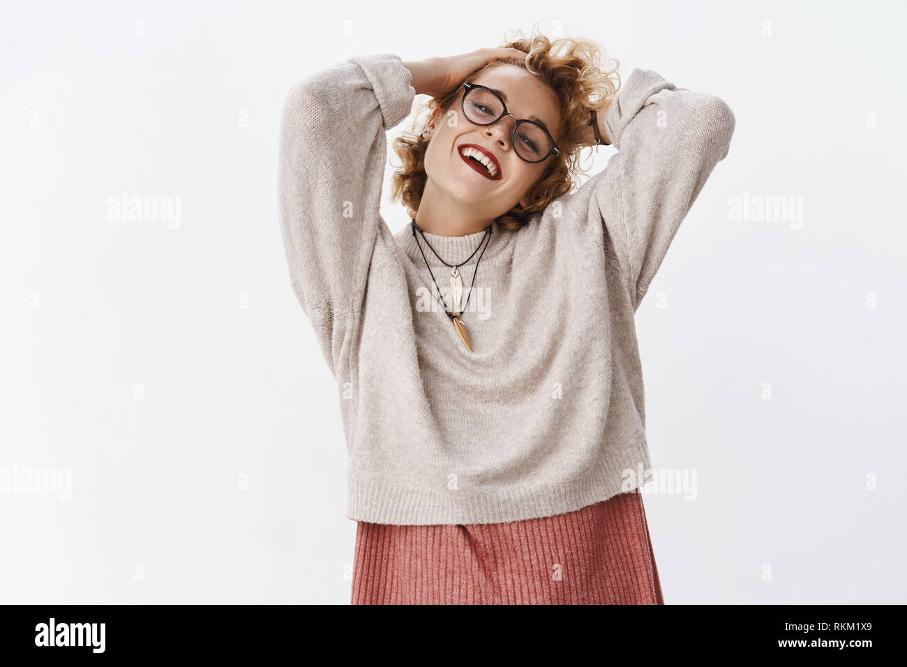 Sentirsi vivi e spensierato. Sollievo gioioso e rilassante bella elegante hipster donna in maglia e bicchieri posa retro tenendo le mani dietro Foto Stock