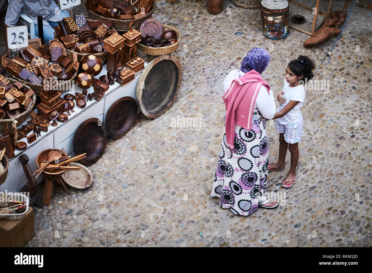 Una donna e bambino stare accanto a un mercato ancora di legname ninnoli e giocattoli in un souq medina di Essaouira, Marocco. Foto Stock