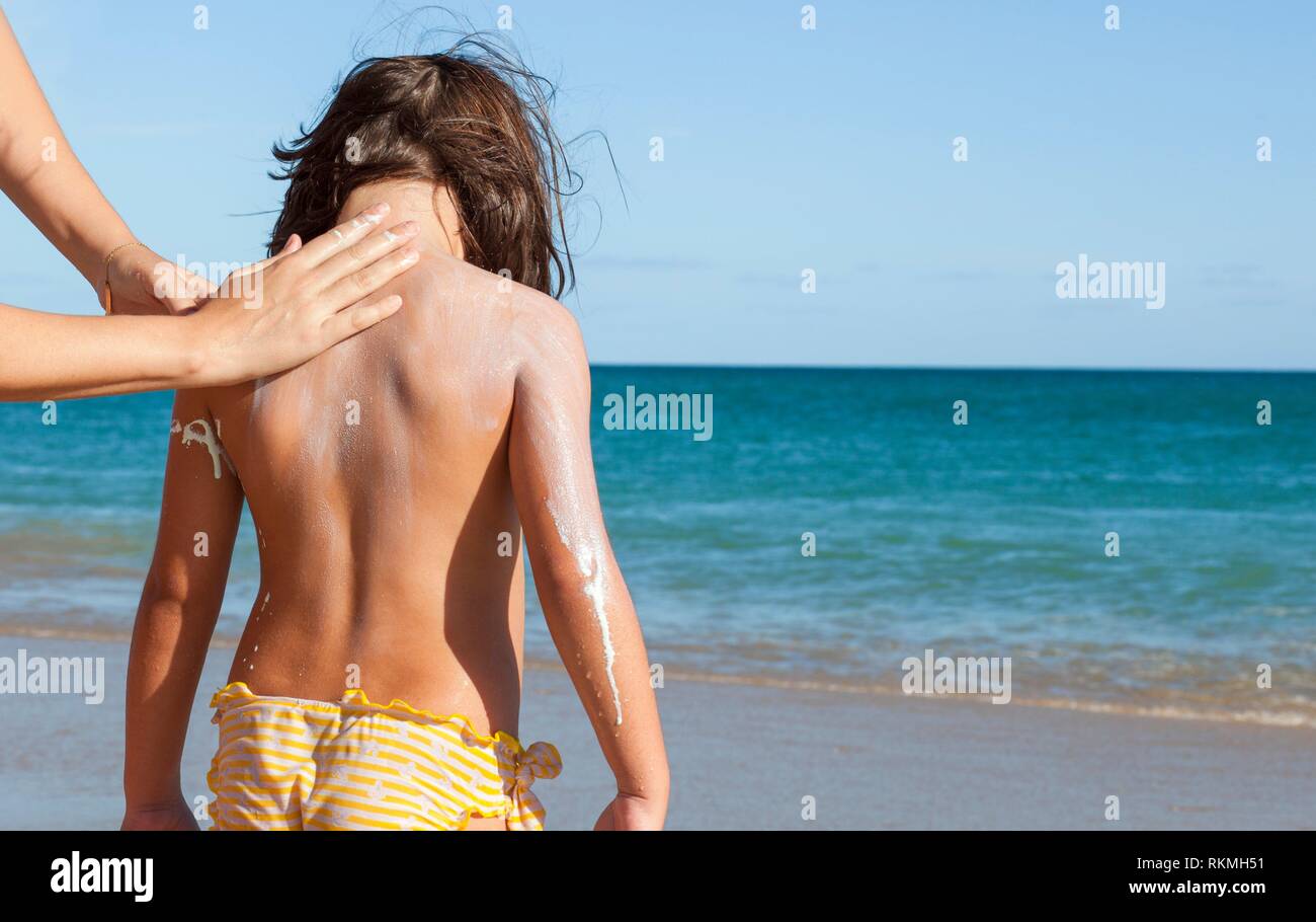 Madre l'applicazione di crema di protezione solare a sua figlia sulla nuca. Spiaggia idilliaca sfondo. Foto Stock