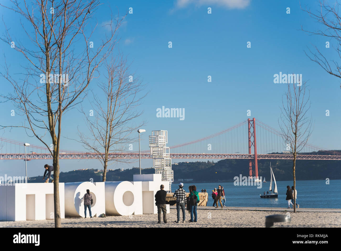 Lisbona, Portogallo - 12/28/18: logo Maat scultura fuori di museo a Belem, le persone aventi il divertimento, camminando con red 25 aprile ponte sul fiume Tago di imbarcazioni a vela Foto Stock
