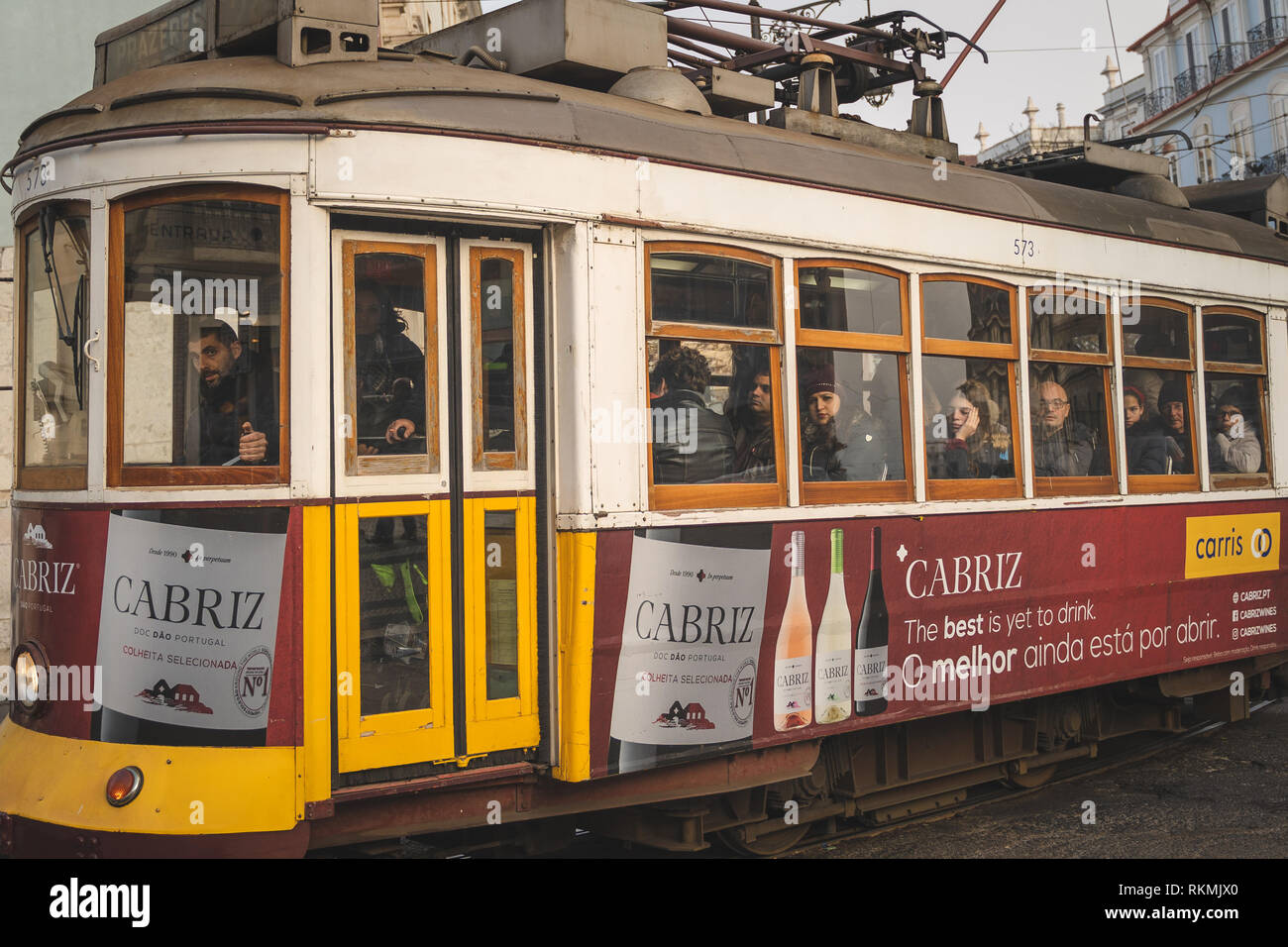 Lisbona, Portogallo - 01/03/19: Tradizionale giallo vecchio tram elettrico nel centro di Lisbona. Vista laterale con passeggeri e windows, vino Cabriz annuncio Foto Stock