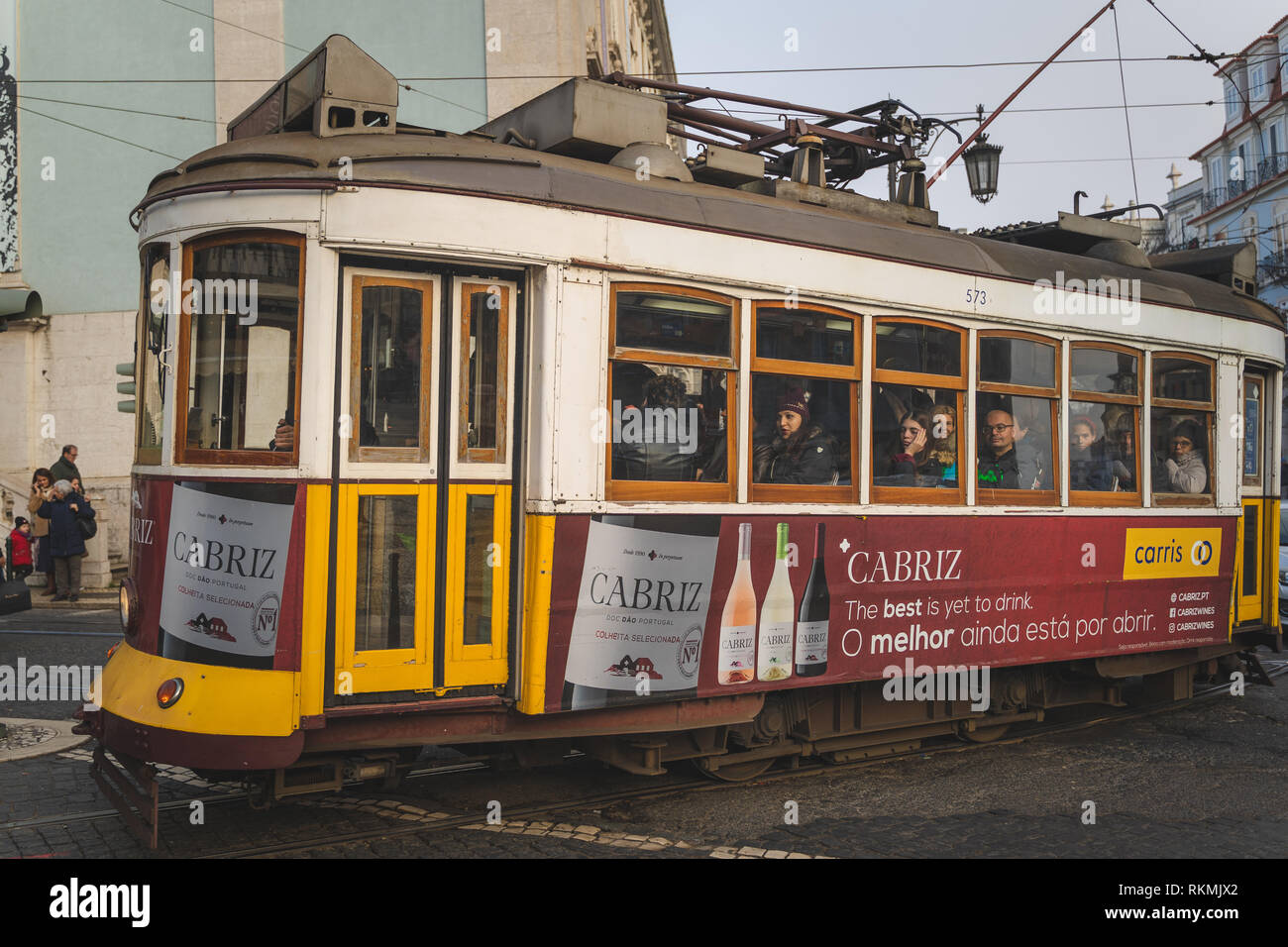 Lisbona, Portogallo - 01/03/19: Tradizionale giallo vecchio tram elettrico nel centro di Lisbona. Vista laterale con passeggeri e windows, vino Cabriz annuncio Foto Stock