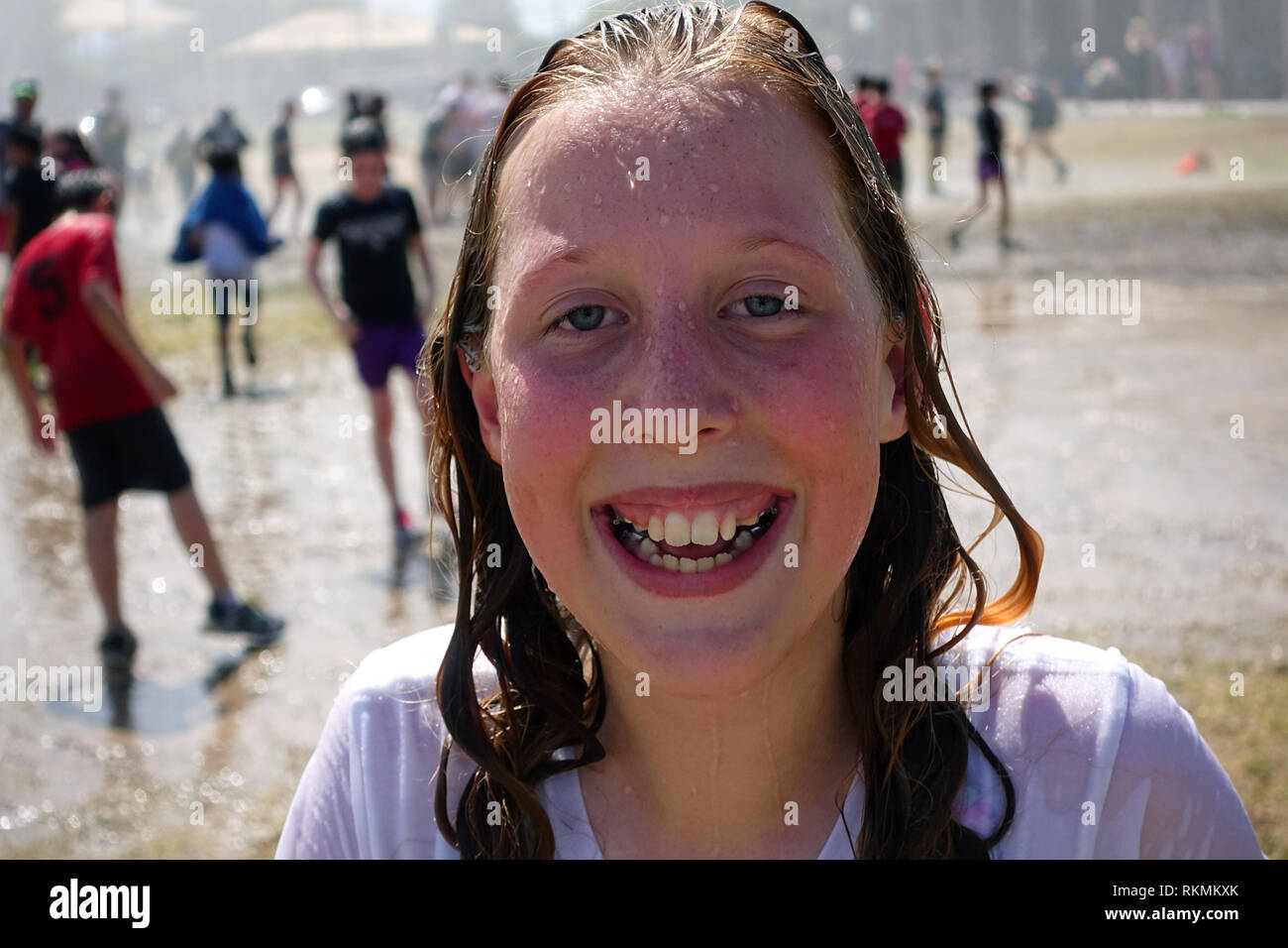 Una grade School girl condivide un sorriso mentre bagnarvi mentre giocando nel parco giochi. Foto Stock