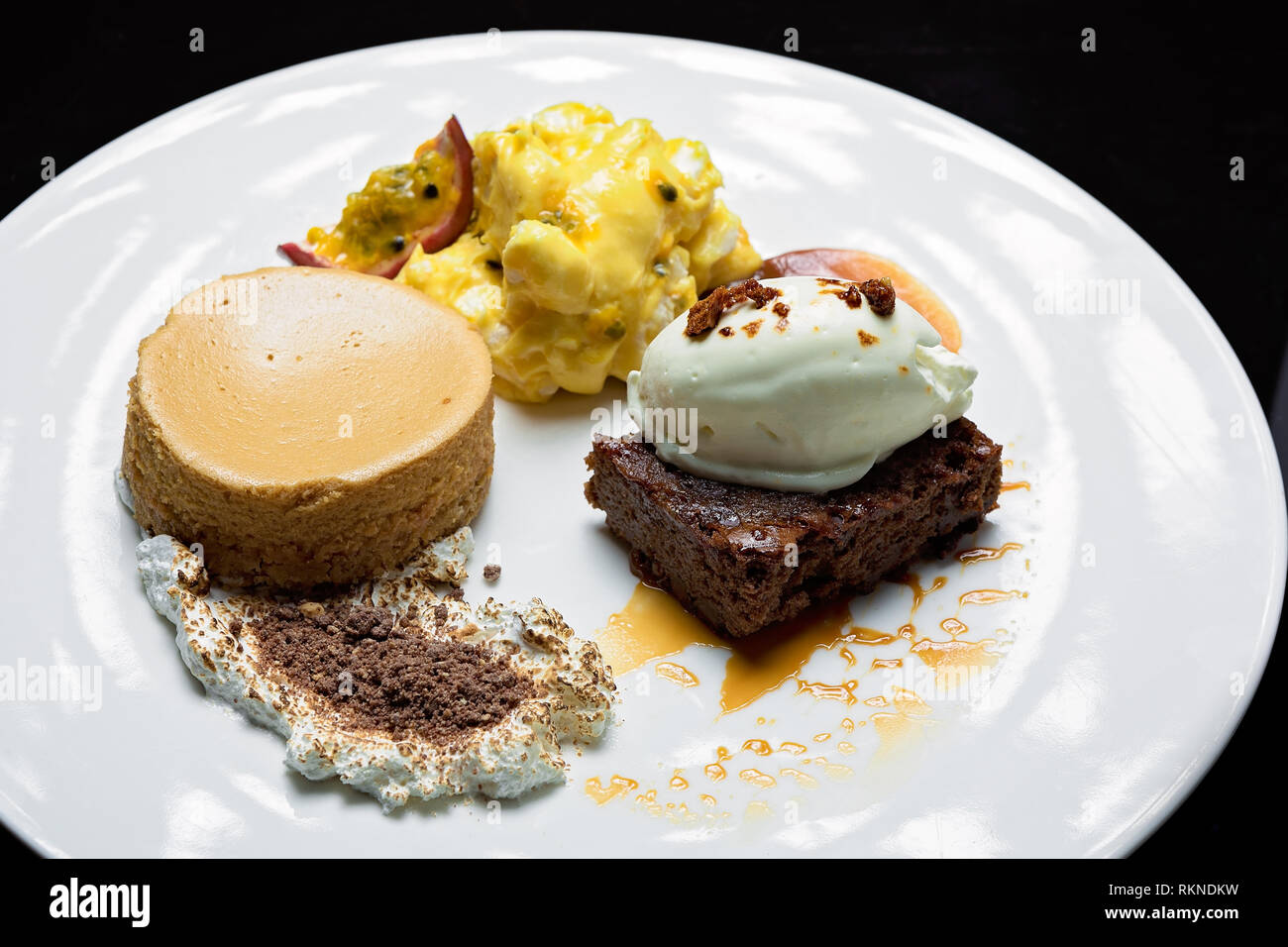 Selezione di dessert composta da una brownie al cioccolato servita con un cucchiaio di iceam, una torta al caramello servita una purea di frutta fresca e crema. Foto Stock