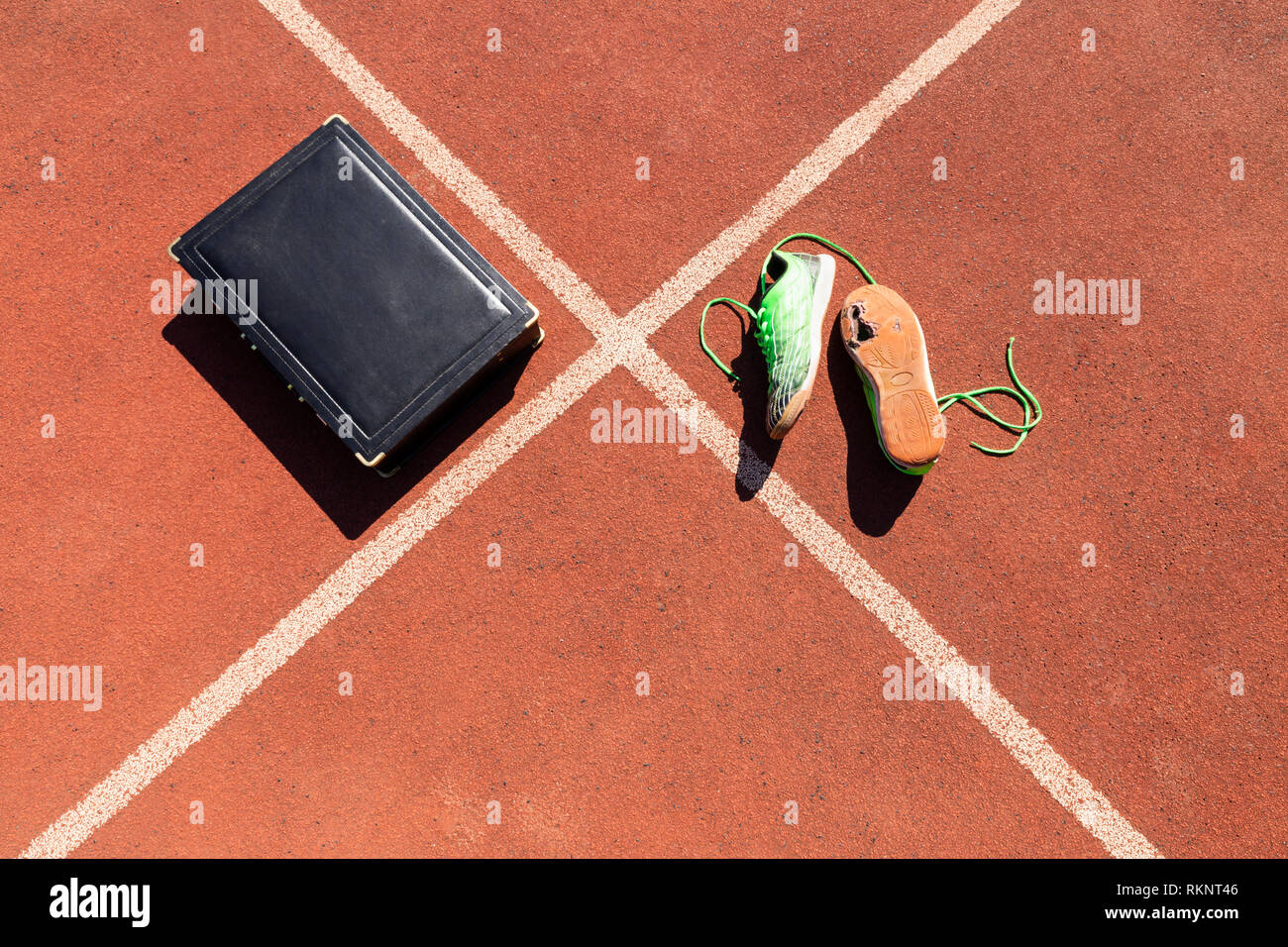 Una ventiquattrore nera e un paio di rotture di green scarpe da corsa su una via di corsa che simbolizza la concorrenza, sfida e burnout nel lavoro e affari. Foto Stock