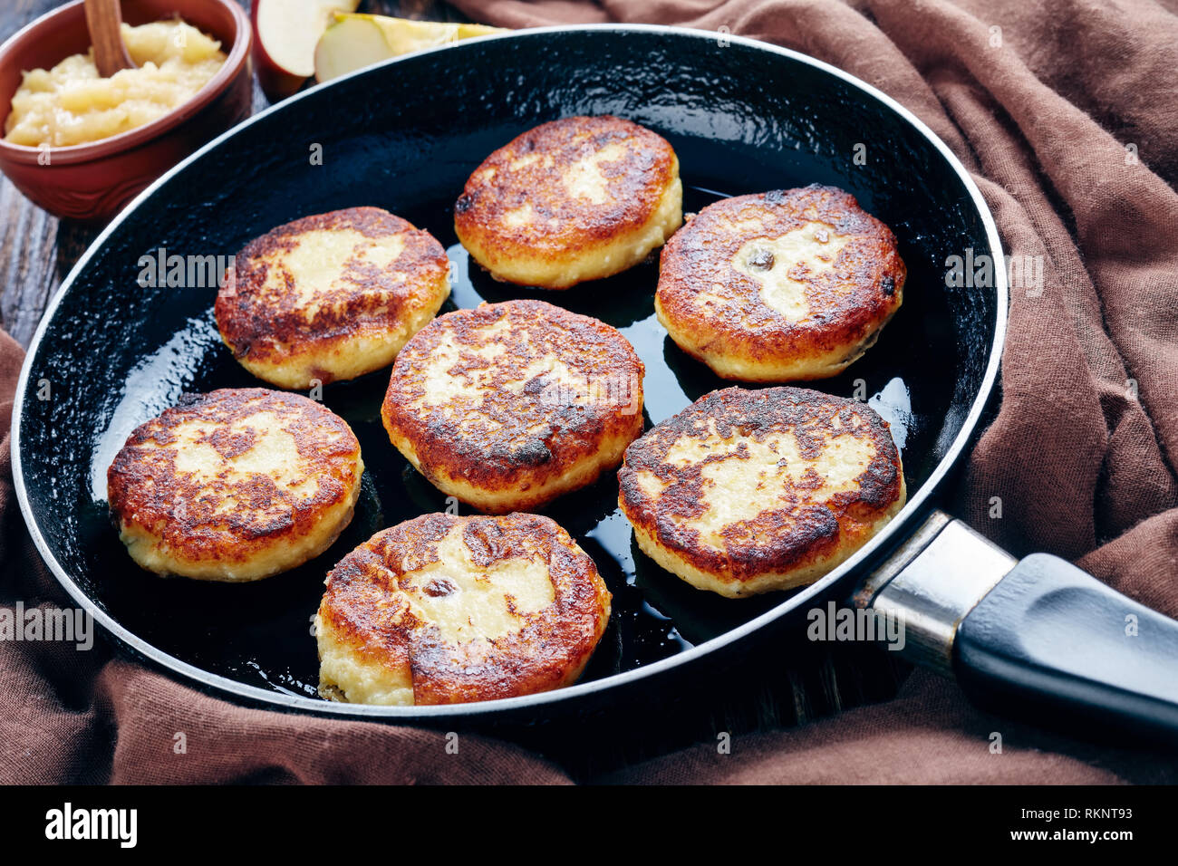 Delizioso cottage cheese frittelle di patate con uvetta - Quarkkeulchen in una padella su un vecchio tavolo in legno marrone con un panno e mousse di Apple in una ciotola, Foto Stock