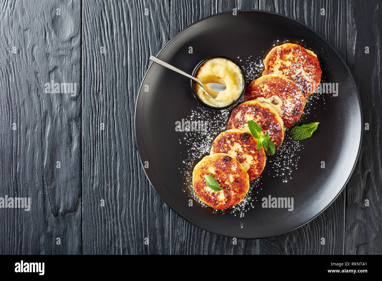 Il tedesco quark frittelle di patate - Quarkkeulchen spolverati con zucchero a velo e decorate con foglie di menta su un piatto nero con mousse di apple, visualizzare f Foto Stock