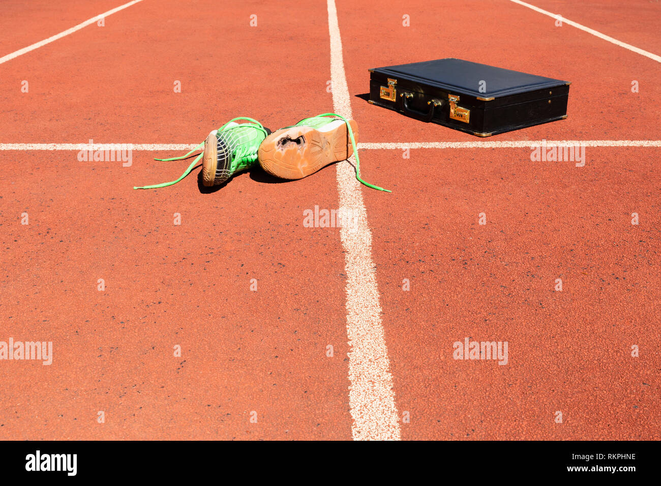 Una ventiquattrore nera e un paio di rotture di green scarpe da corsa su una via di corsa che simbolizza la concorrenza, sfida e burnout nel lavoro e affari. Foto Stock