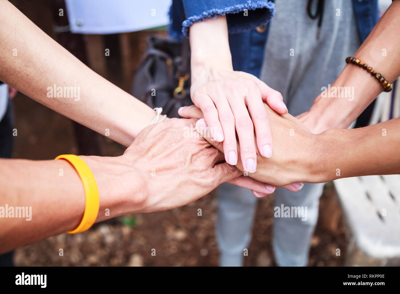 Giovani uomini e donne in piedi e mani di impilaggio in una riunione sul suolo naturale background in gita all'aperto. Il lavoro di squadra, la diversità, la collaborazione dei giovani Foto Stock