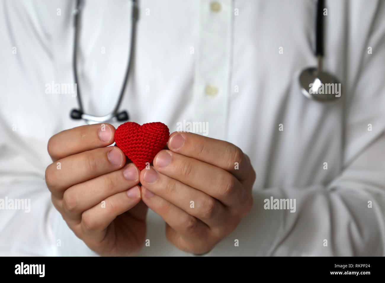 Medico con stetoscopio in azienda a maglia rossa cuore nelle mani. Concetto di cardiologia, le malattie di cuore, diagnosi, esame medico in clinica Foto Stock
