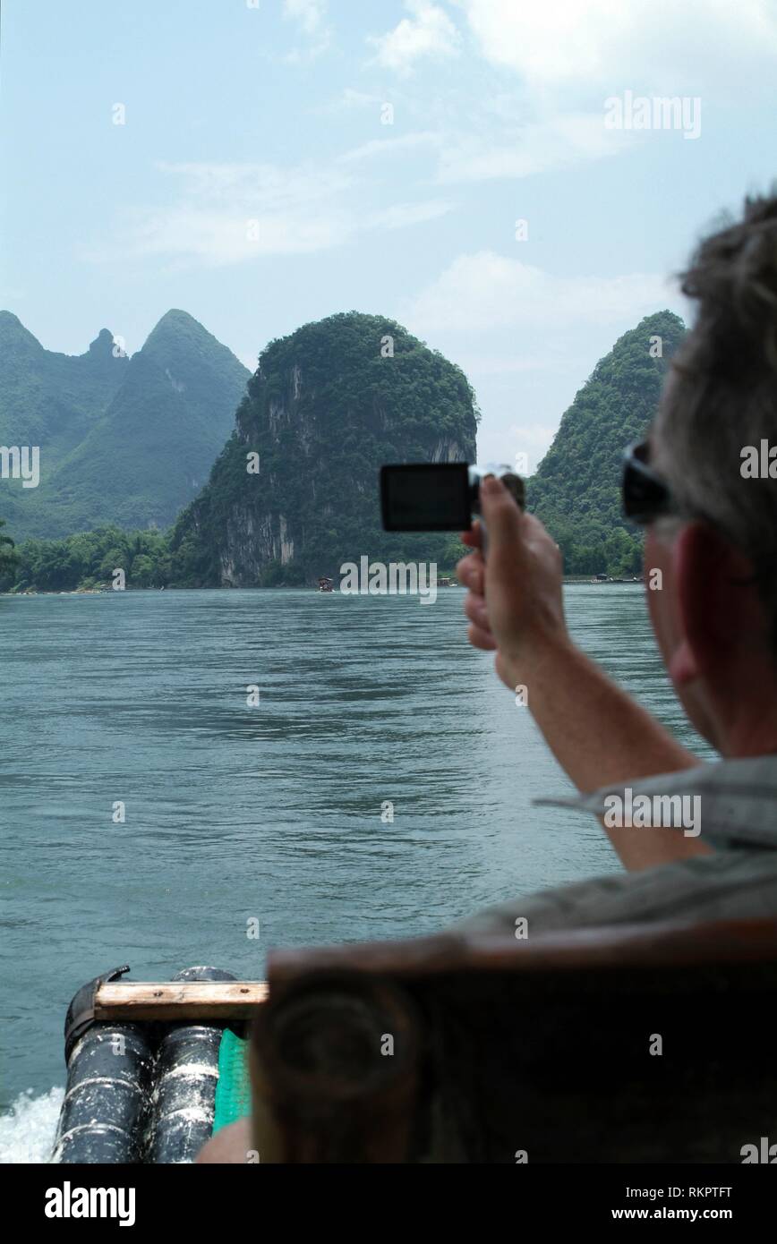 Un turista fotografie lo spettacolare paesaggio lungo il Fiume Li mentre galleggiante su una zattera di bamboo in Yangshuo. Chiazzato con montagne carsiche e la ge Foto Stock