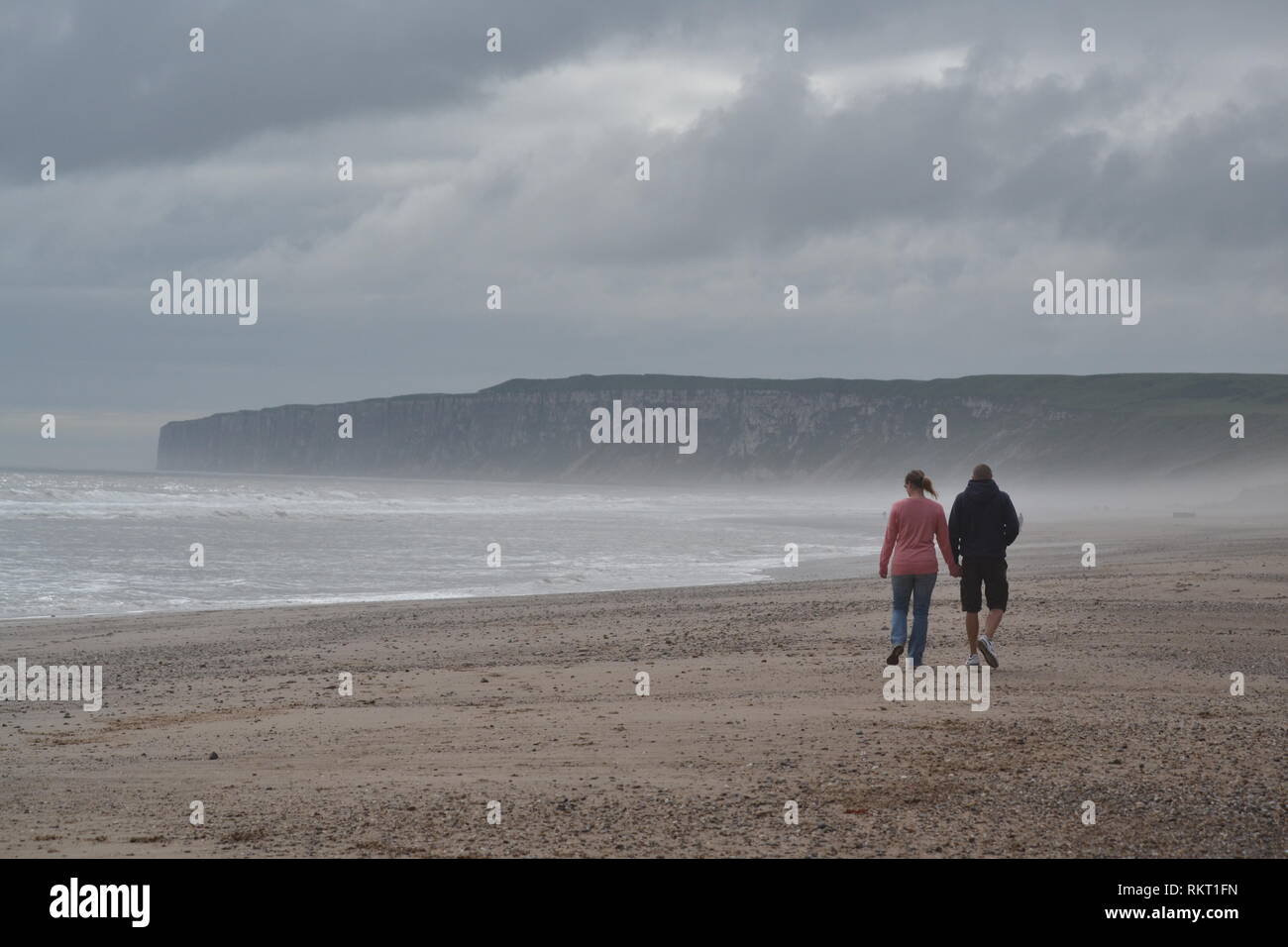 Giovane holding hands passeggiando lungo la spiaggia su una mattina nuvoloso. Hunmanby Gap e Mare del Nord Filey Yorkshire Foto Stock