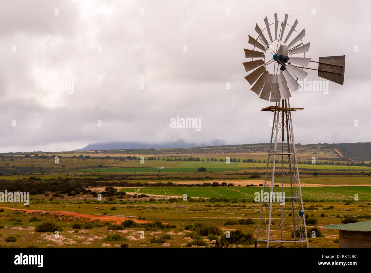 Un mulino a vento di metallo della pompa dell'acqua insieme contro i campi e un cielo tempestoso. Western Cape, Sud Africa. Foto Stock