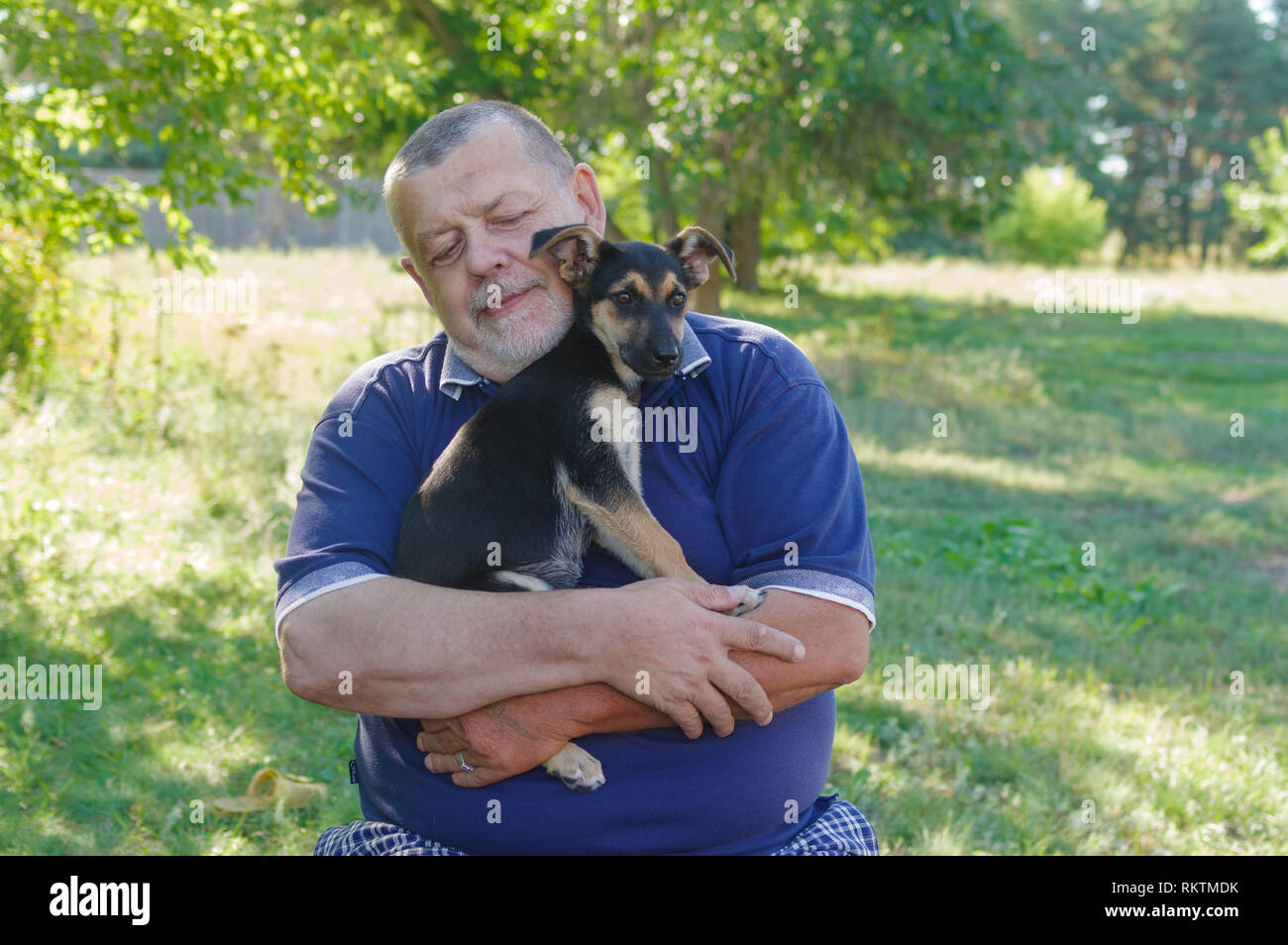 Outdoor ritratto del Caucaso uomo senior rilassante mentre si tiene il nero piccolo cucciolo sulle mani Foto Stock