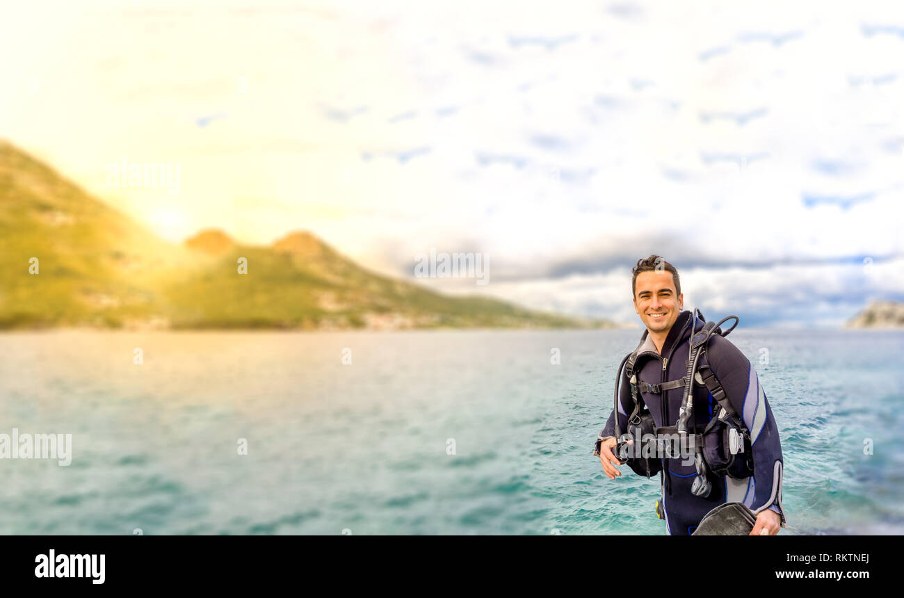 Giovane uomo bello isolato diver sorridente pronto a fare immersioni in acqua fredda muta, alette, peso belt & oxigen ingranaggio in Karaburun, Izmir. Turchia Foto Stock